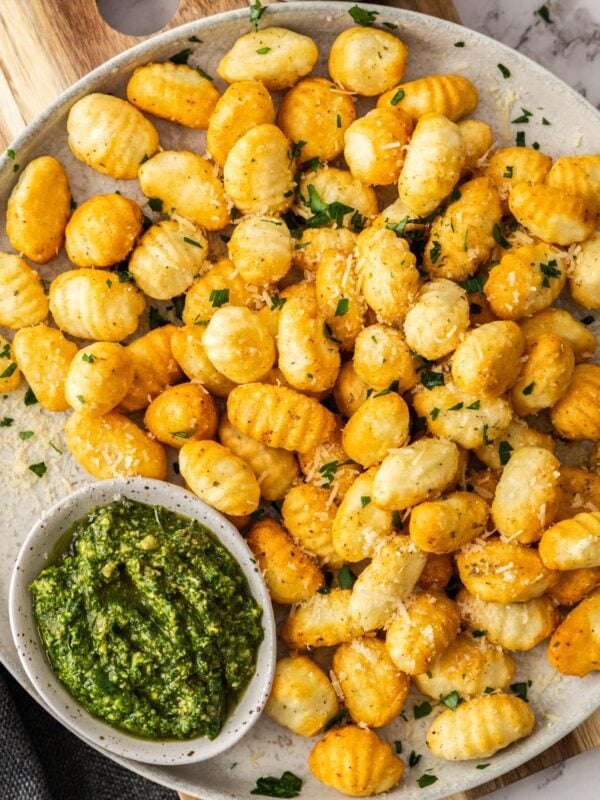 a grey dish with crispy air fryer gnocchi topped with chopped parsley. There are bowls of pesto and marinara.