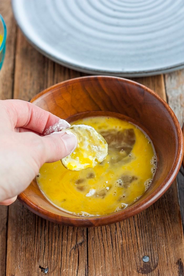 a hand dipping a pickle into a bowl of eggs.
