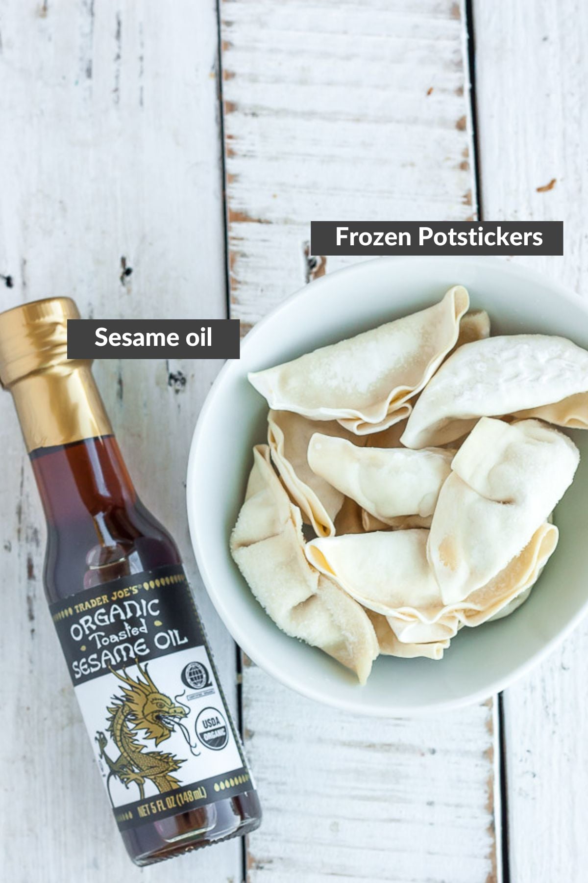 a bowl of frozen potstickers and a bottle of sesame oil on a white wooden board.