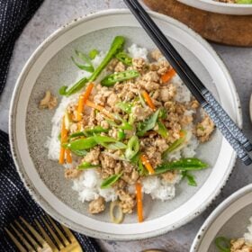 a plate of ground chicken teriyaki topped with veggies and sesame seeds with chopsticks on the plate.