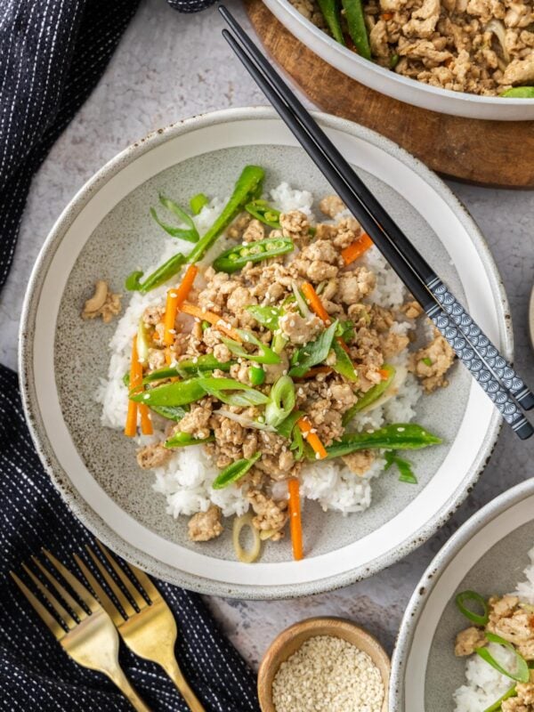 a plate of ground chicken teriyaki topped with veggies and sesame seeds with chopsticks on the plate.