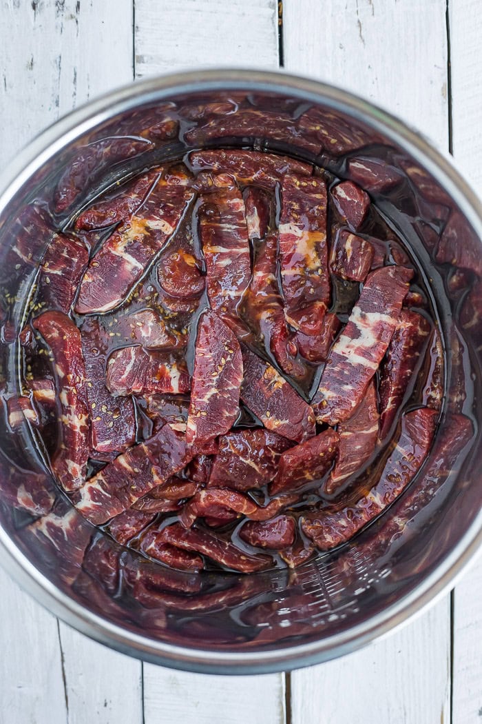 slices of uncooked beef marinated in sauce in a pressure cooker insert.