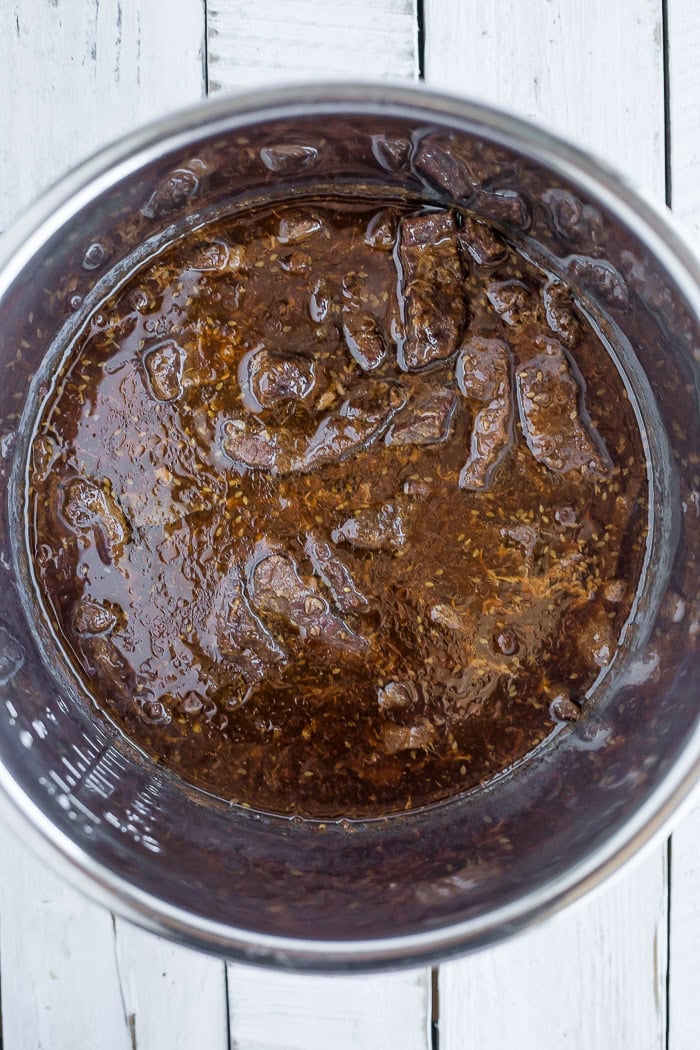 slices of cooked beef in sauce in a pressure cooker insert.