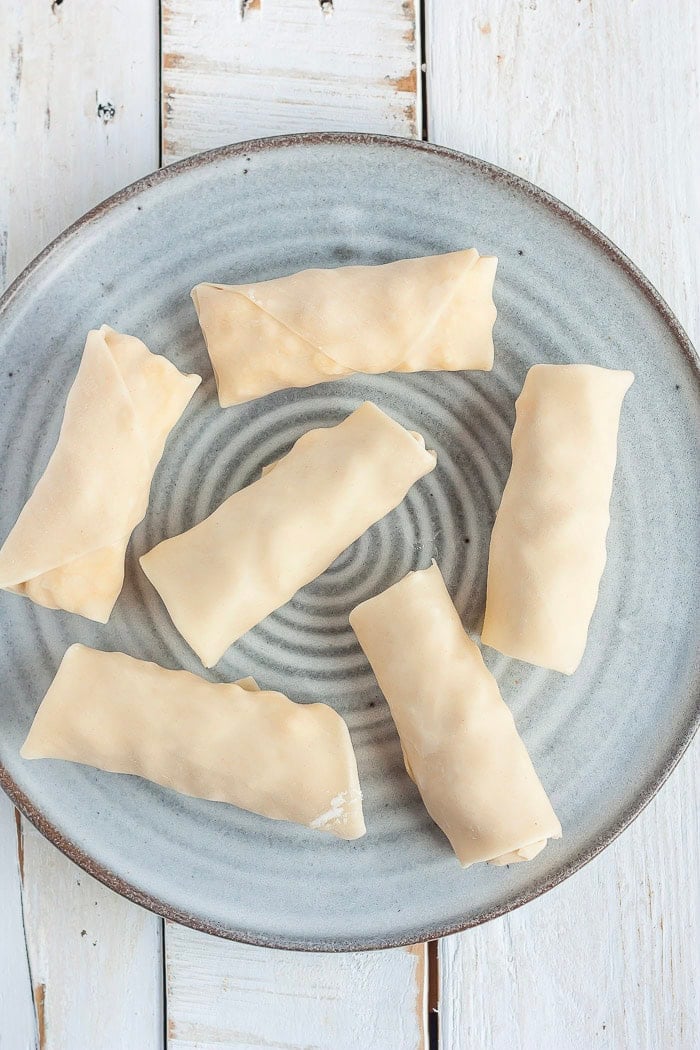 Uncooked spring rolls on a grey plate.