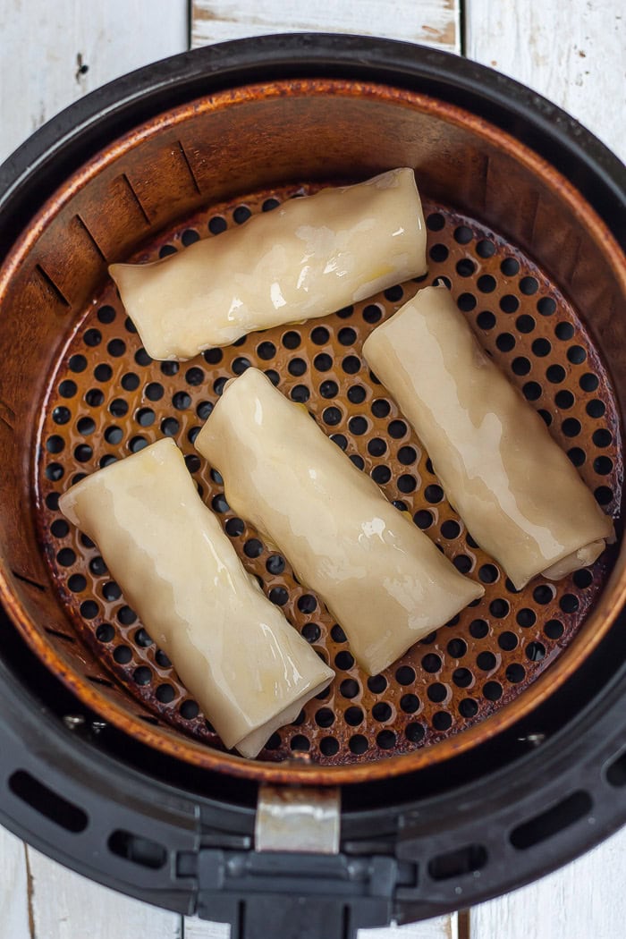 uncooked spring rolls in an air fryer basket.