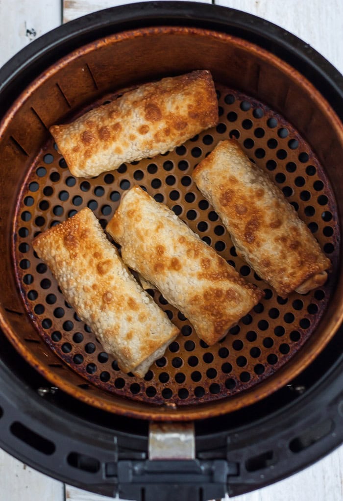 cooked spring rolls in an air fryer basket.