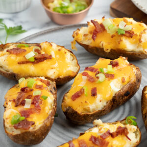 a grey plate with stuffed baked potatoes topped with cheese, bacon, and green onions on it.