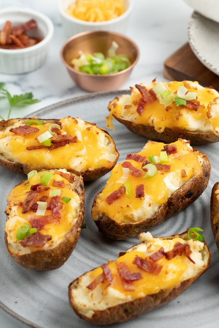 a grey plate with stuffed baked potatoes topped with cheese, bacon, and green onions on it.