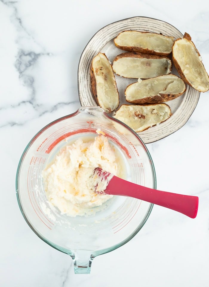 a bowl with a silicone spoon in it and potato skins on a plate.