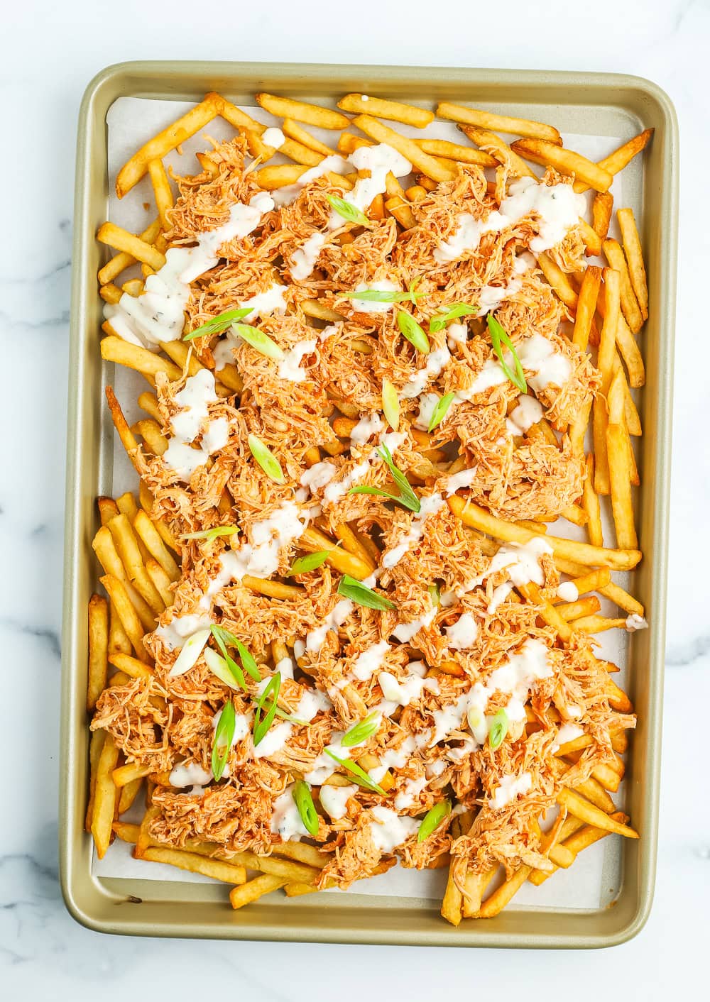 a sheet pan with fries topped with shredded chicken, ranch, and scallions.