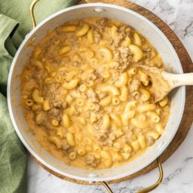 a large saucepan of cheeseburger mac and cheese with a wooden spoon on a marbled board.
