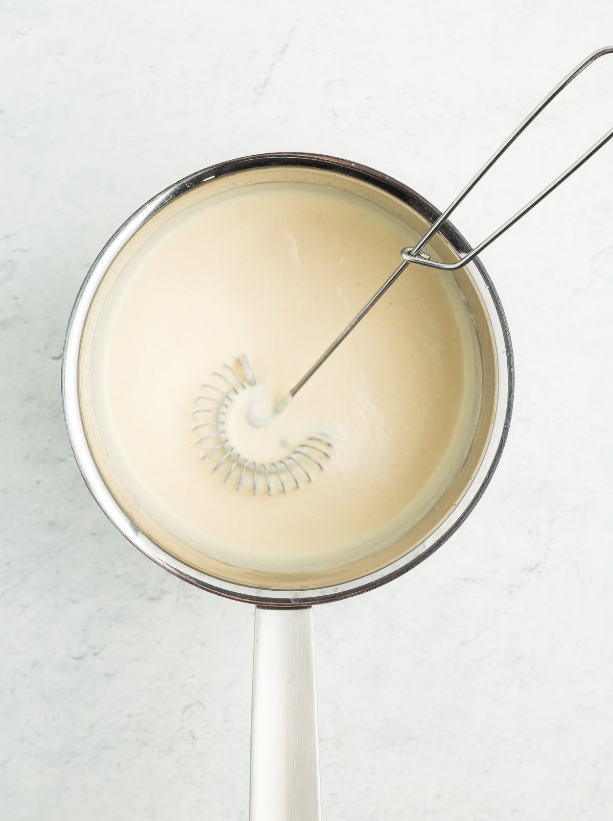a whisk in a saucepan of a white sauce.