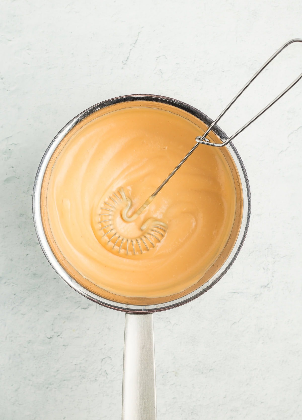 a whisk in a saucepan of cheese sauce.
