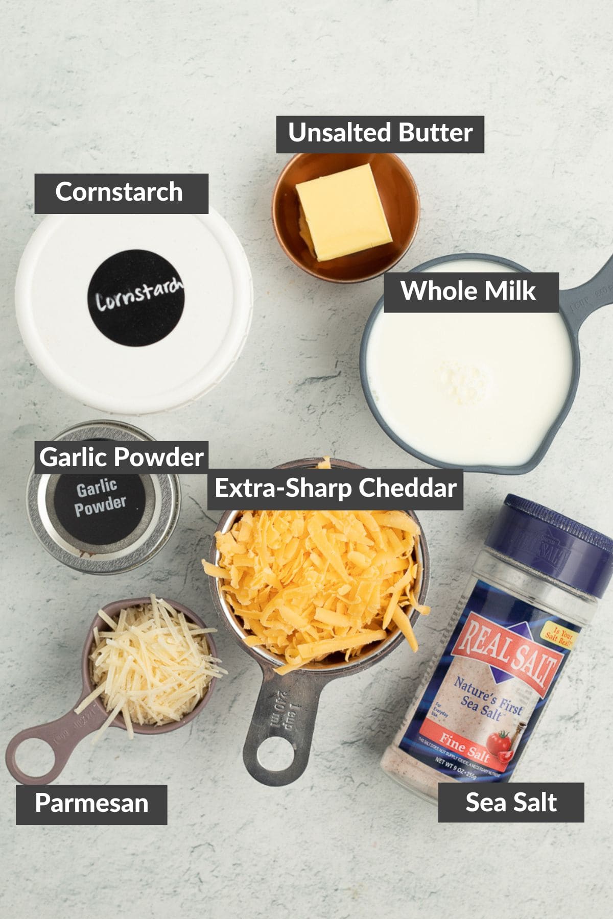 butter, cornstarch, whole milk, extra sharp cheddar, and other ingredients on a grey board.
