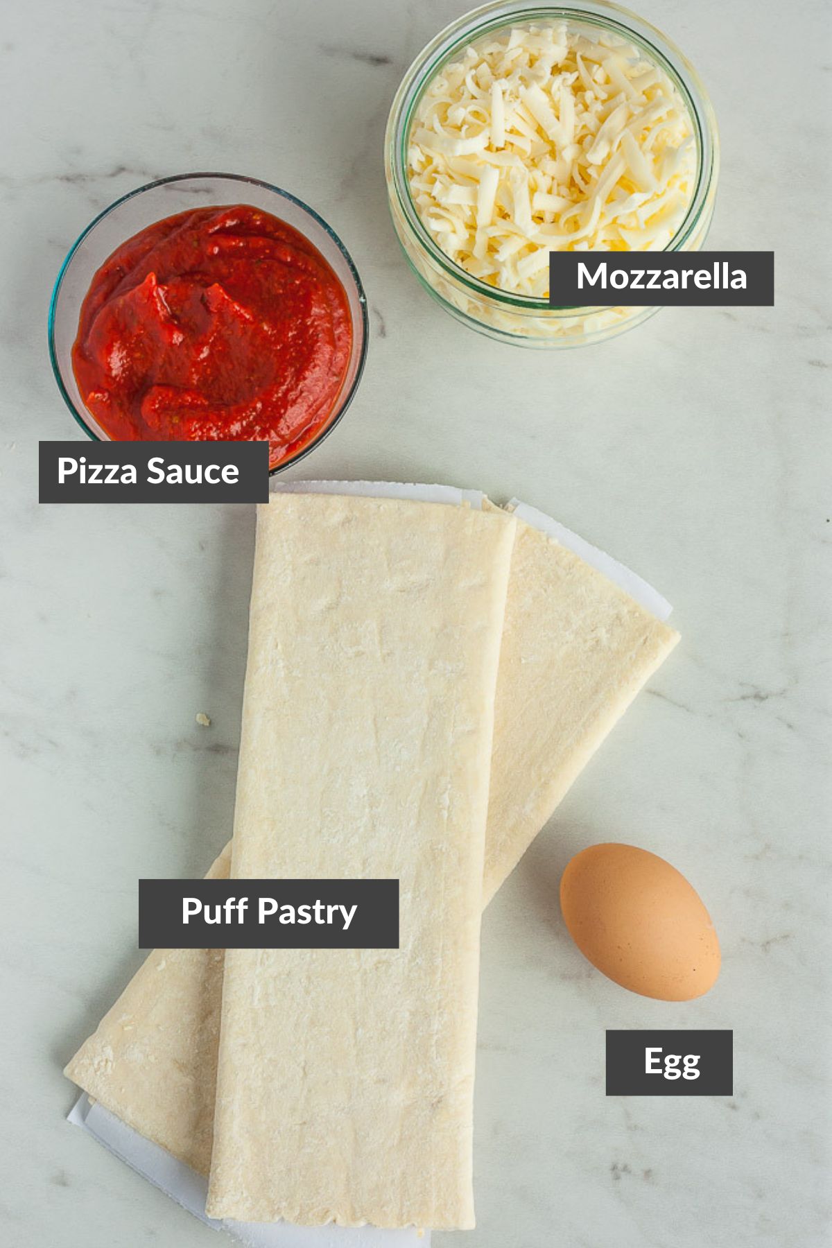 puff pastry, shredded mozzarella, egg, and a bowl of marinara on a marbled board.