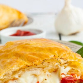 a homemade puff pastry pizza pocket on a plate on a white wooden board.