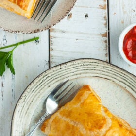 a homemade puff pastry pizza pocket on a plate on a white wooden board.