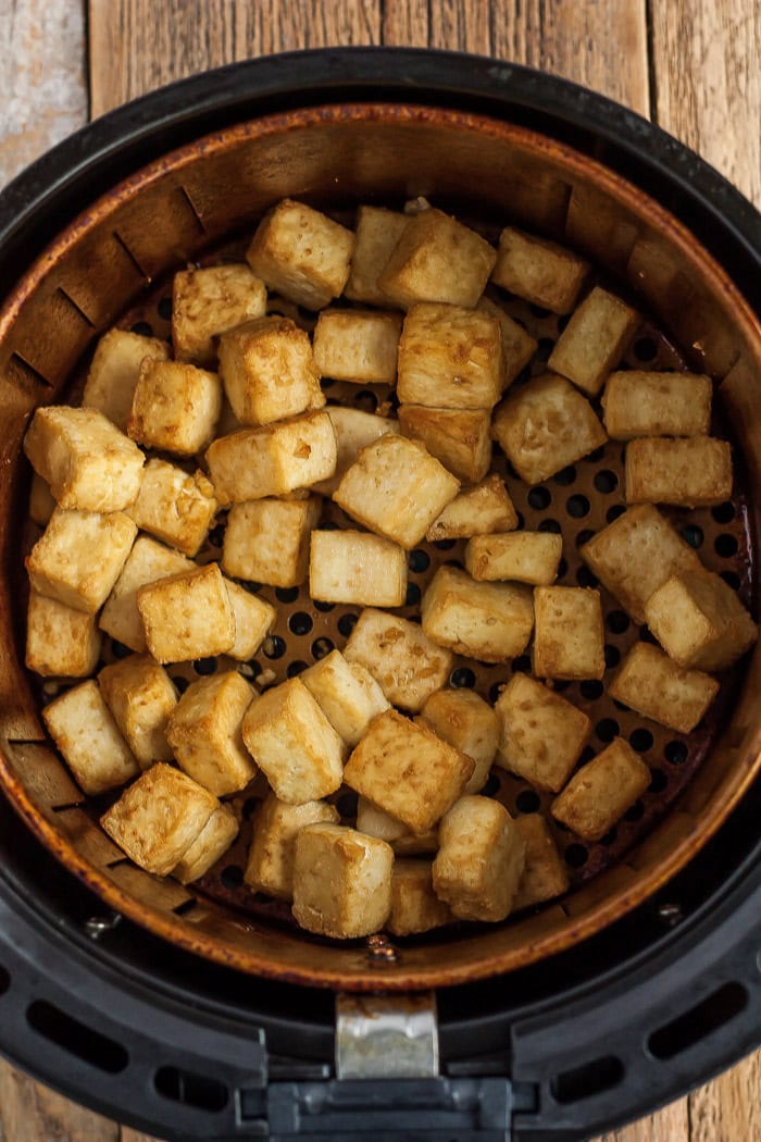 cubes of lightly toasted tofu in an air fryer basket.