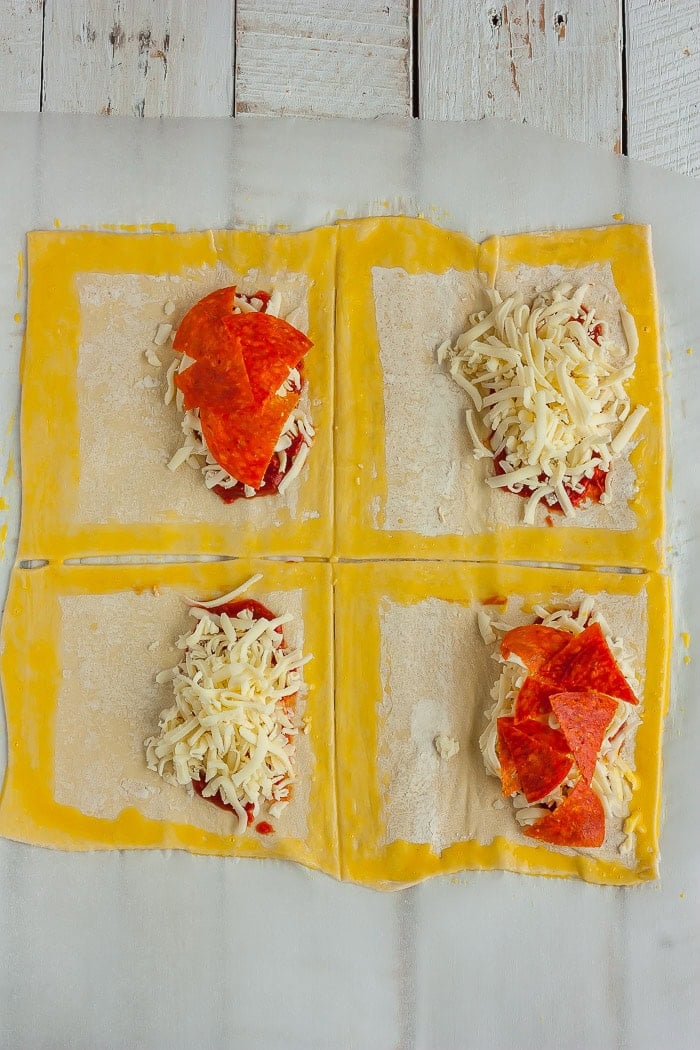 uncooked dough with ingredients and an egg wash on a white wooden board.