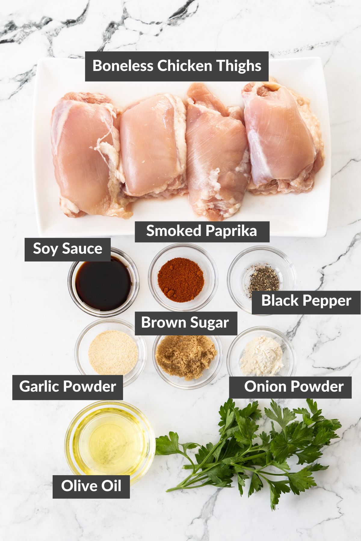 olive oil, soy sauce, parsley, chicken thighs, and other ingredients on a marbled board.