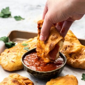 a hand dipping an air fryer calzone into a small bowl of pizza sauce.