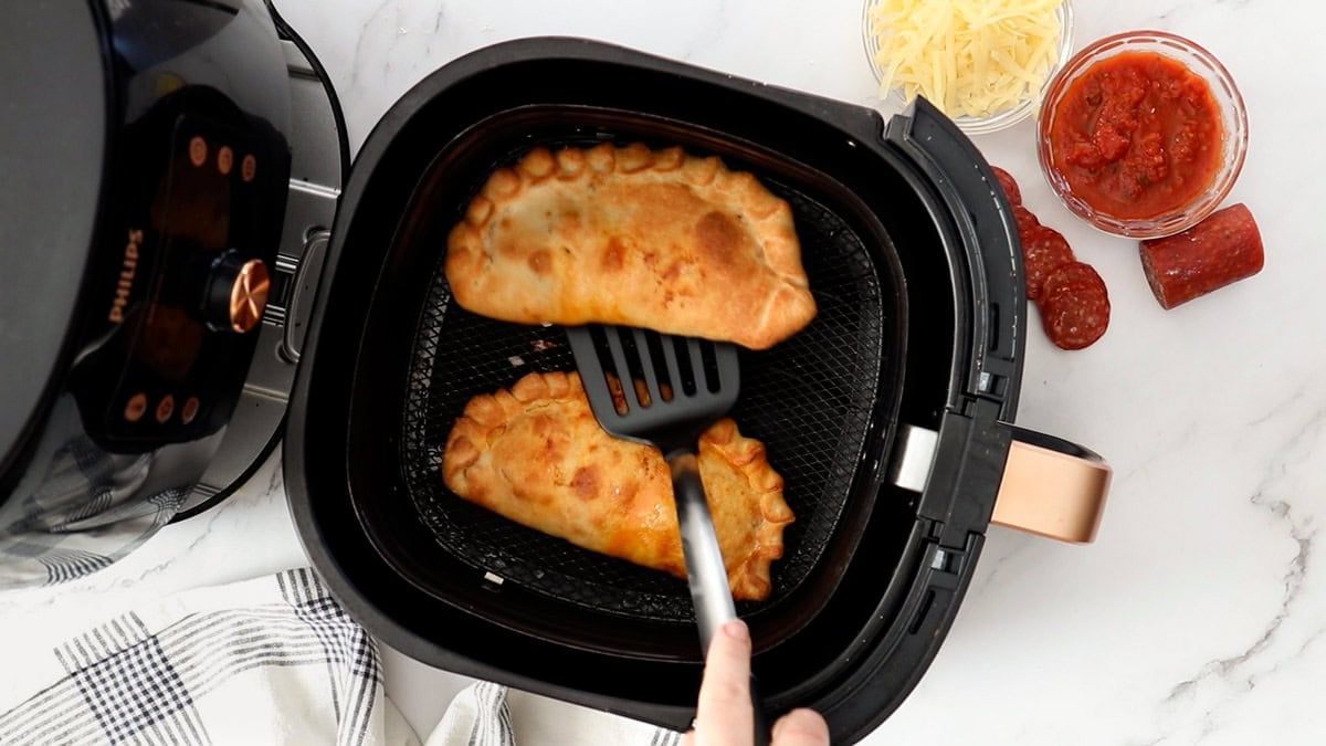 a spatula lifting a cooked calzone out of an air fryer basket.