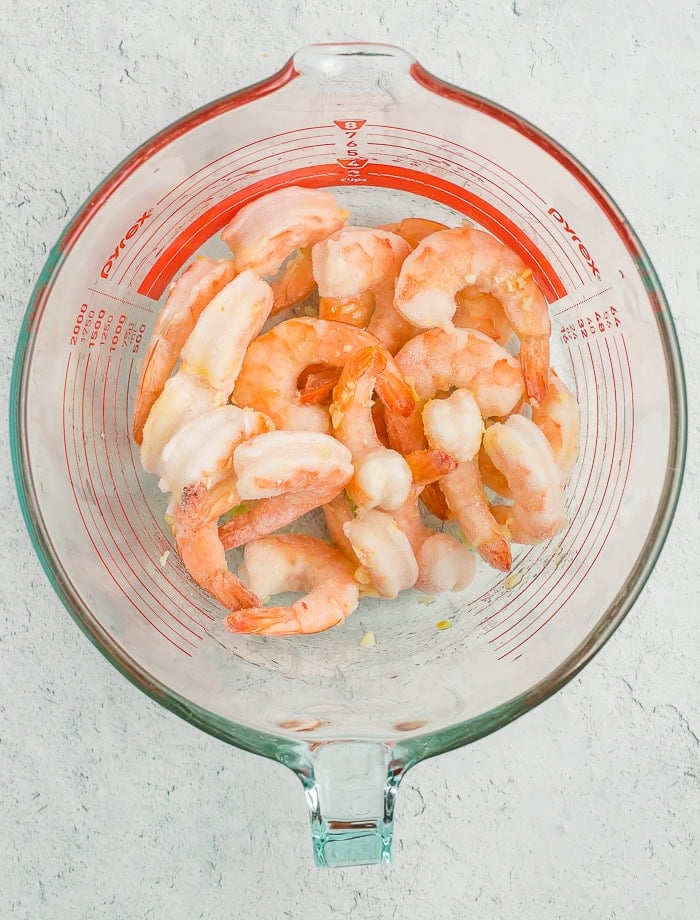 a glass bowl with frozen shrimp tossed in oil and garlic.