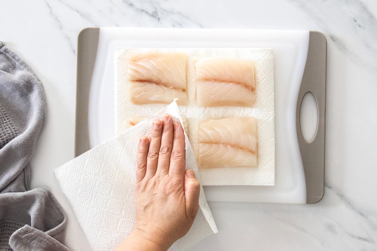 fish being patted dry with paper towels on a white cutting board.