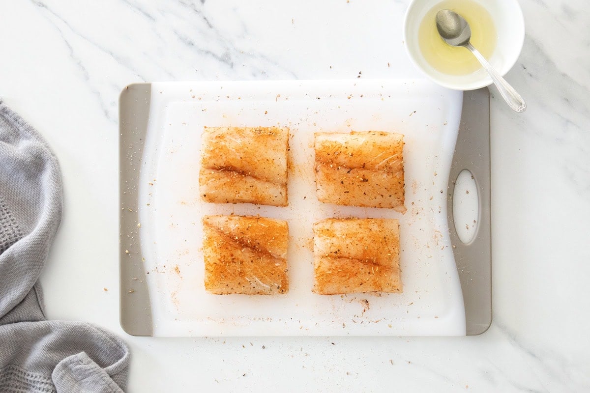 fish filets sitting on a cutting board topped with seasoning.