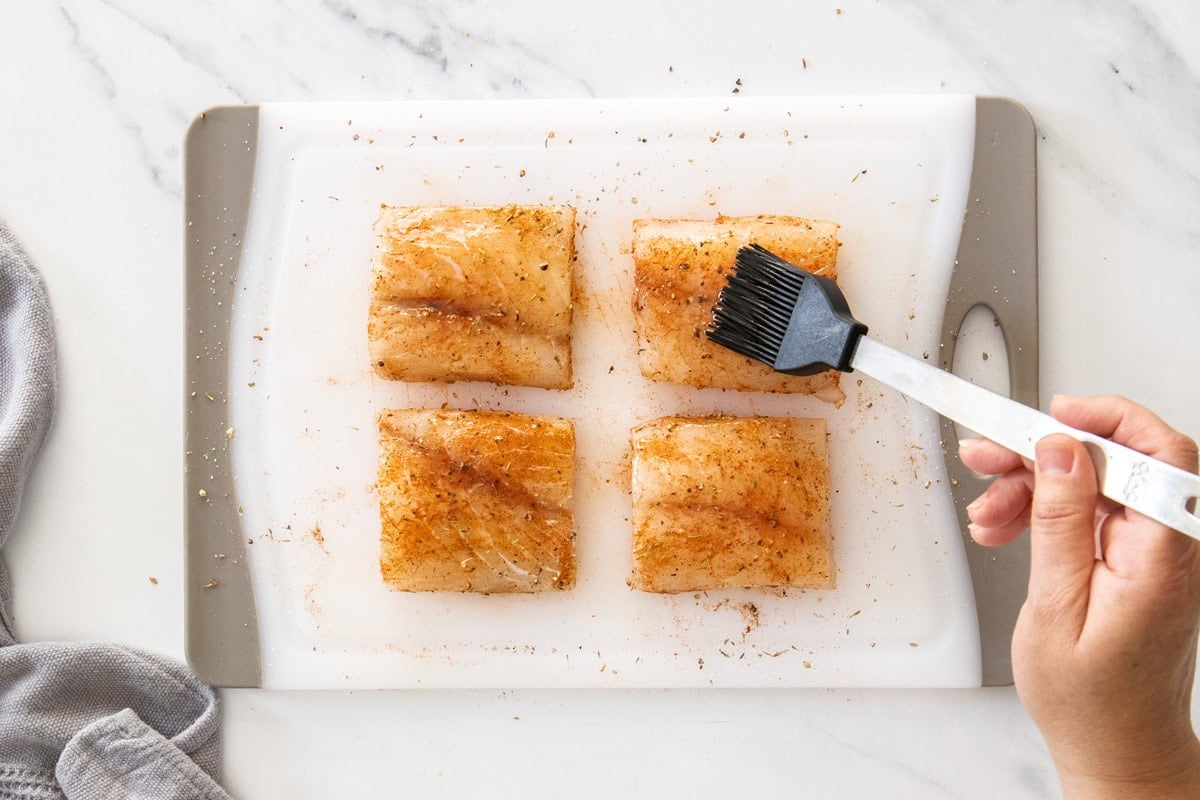 a pastry brush brushing oil on fish filets on a cutting board.
