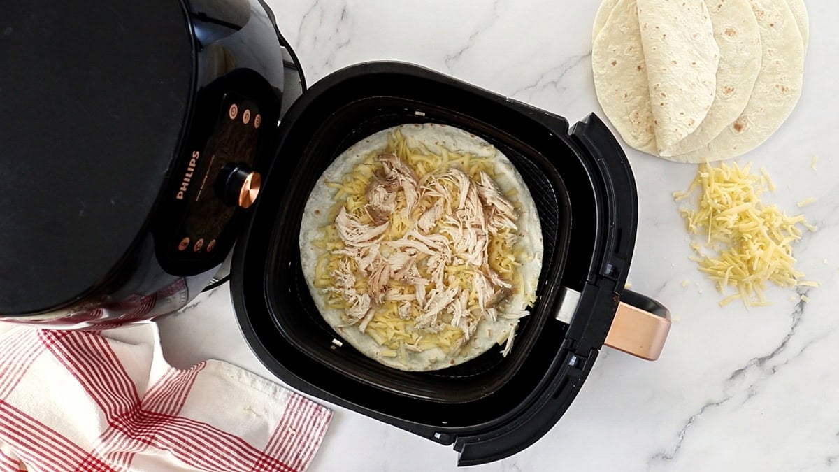 a tortilla topped with cheese and shredded chicken.