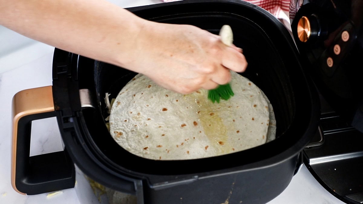 a hand brushing oil on top of a tortilla.