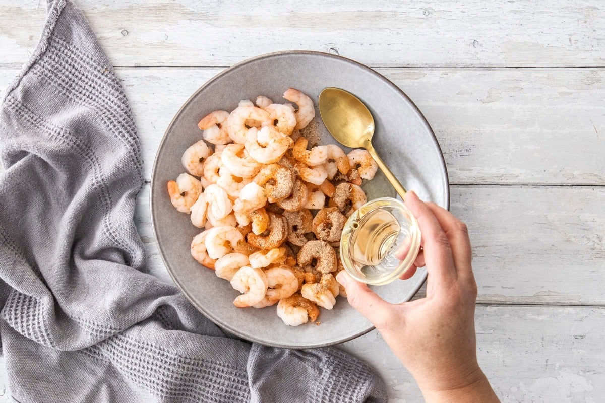 a small bowl of liquid being poured over a bowl of prawns.