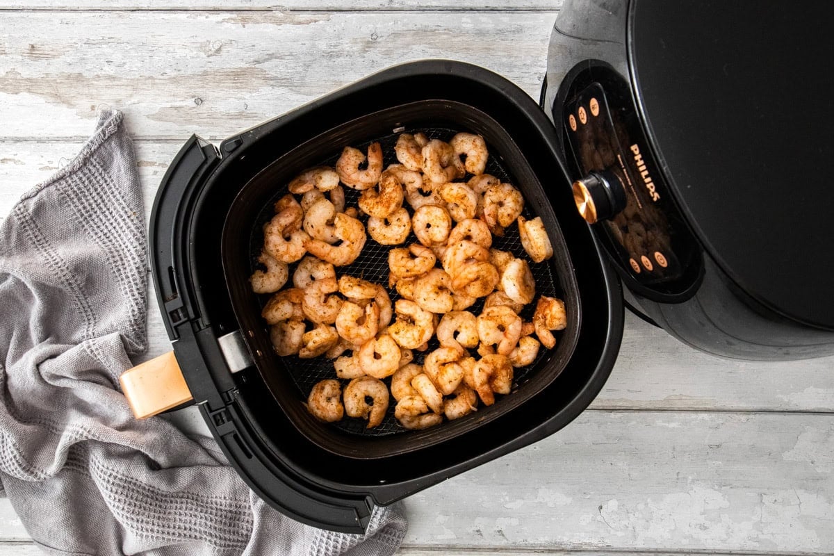 seasoned prawns in an air fryer basket.