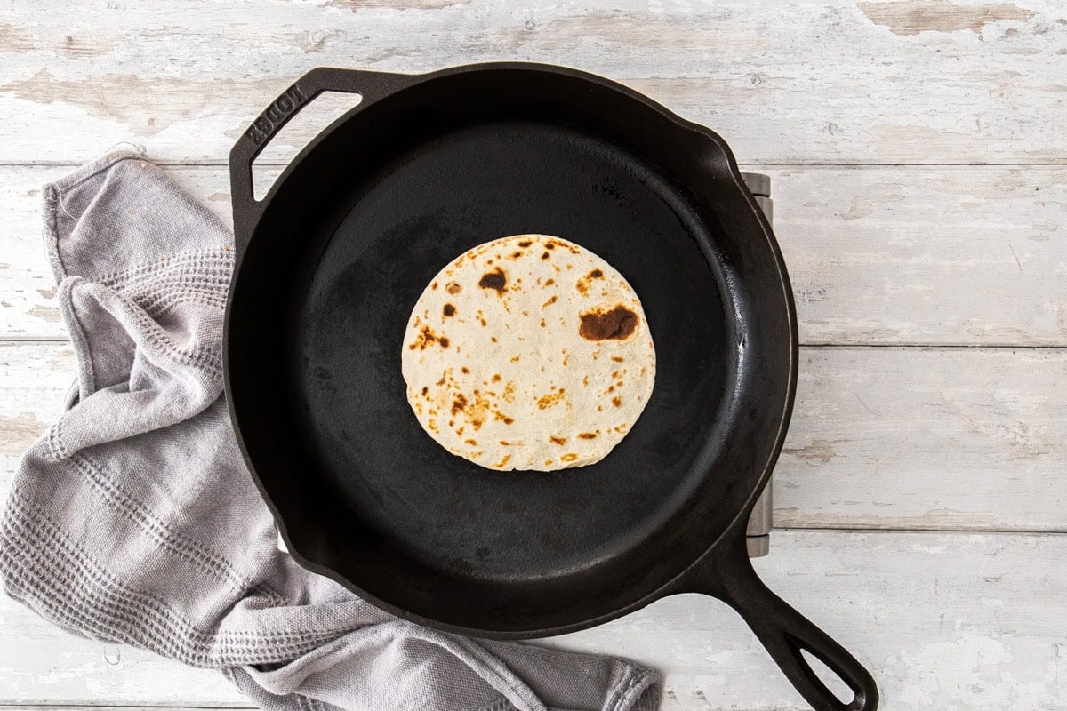 a small street-taco sized tortilla in a cast iron skillet.
