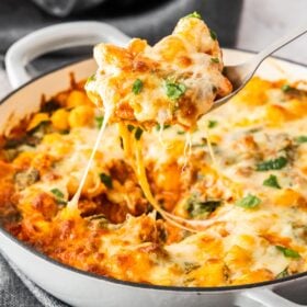 a spoon holding a scoop of gnocchi casserole over a baking dish, with cheese being pulled.