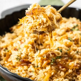 a spoonful of French onion rice being scooped out of a black skillet.