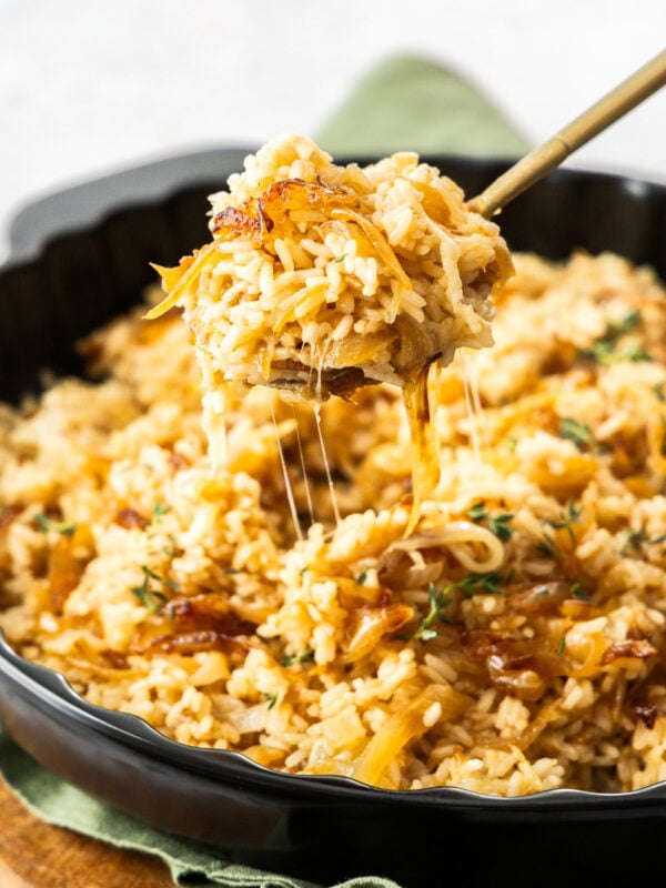 a spoonful of French onion rice being scooped out of a black skillet.