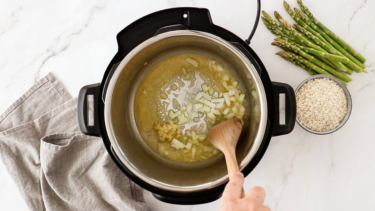 onions and garlic being sauteed in butter in a pressure cooker.