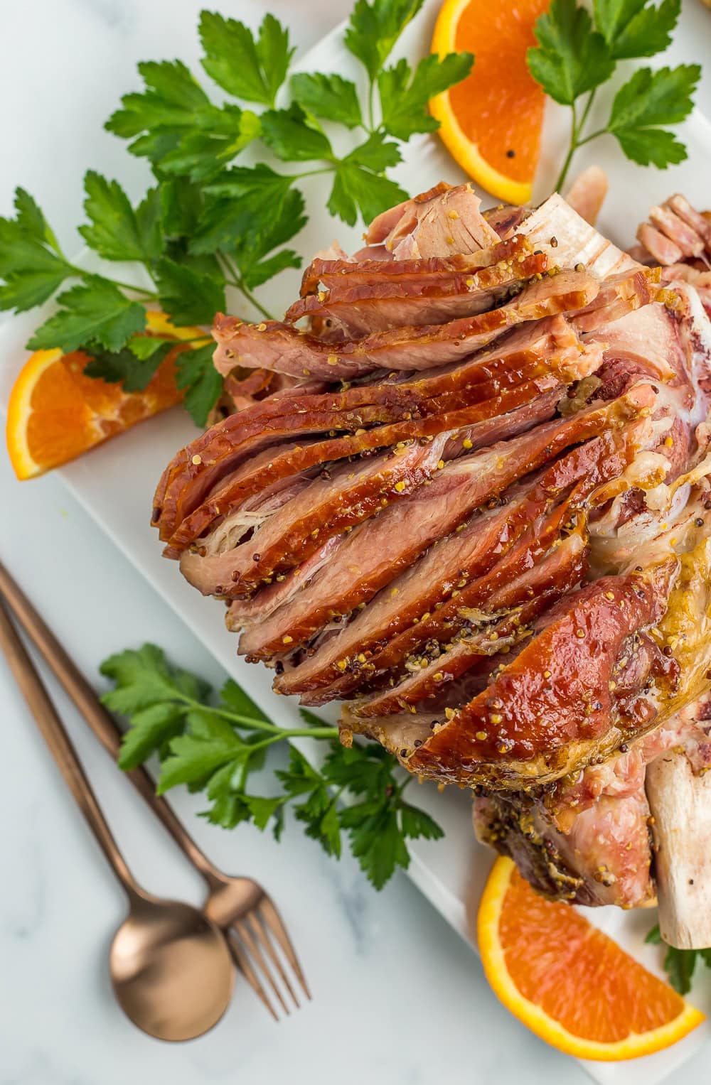 a spiral cut ham on a white platter with parsley and sliced oranges.