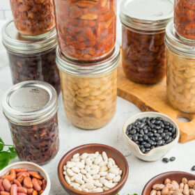 8 jars of canned beans with small bowls of dried beans.