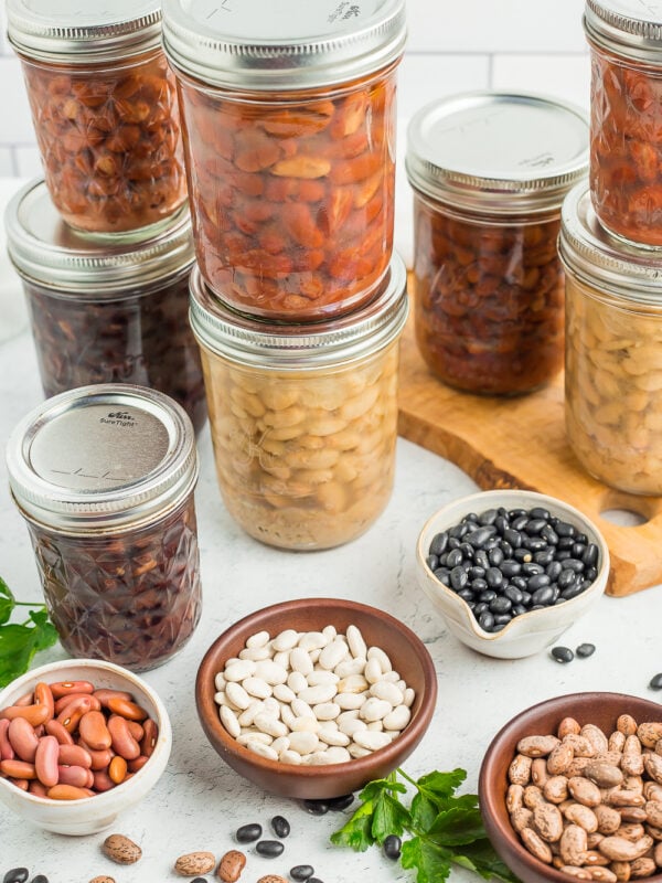 8 jars of canned beans with small bowls of dried beans.