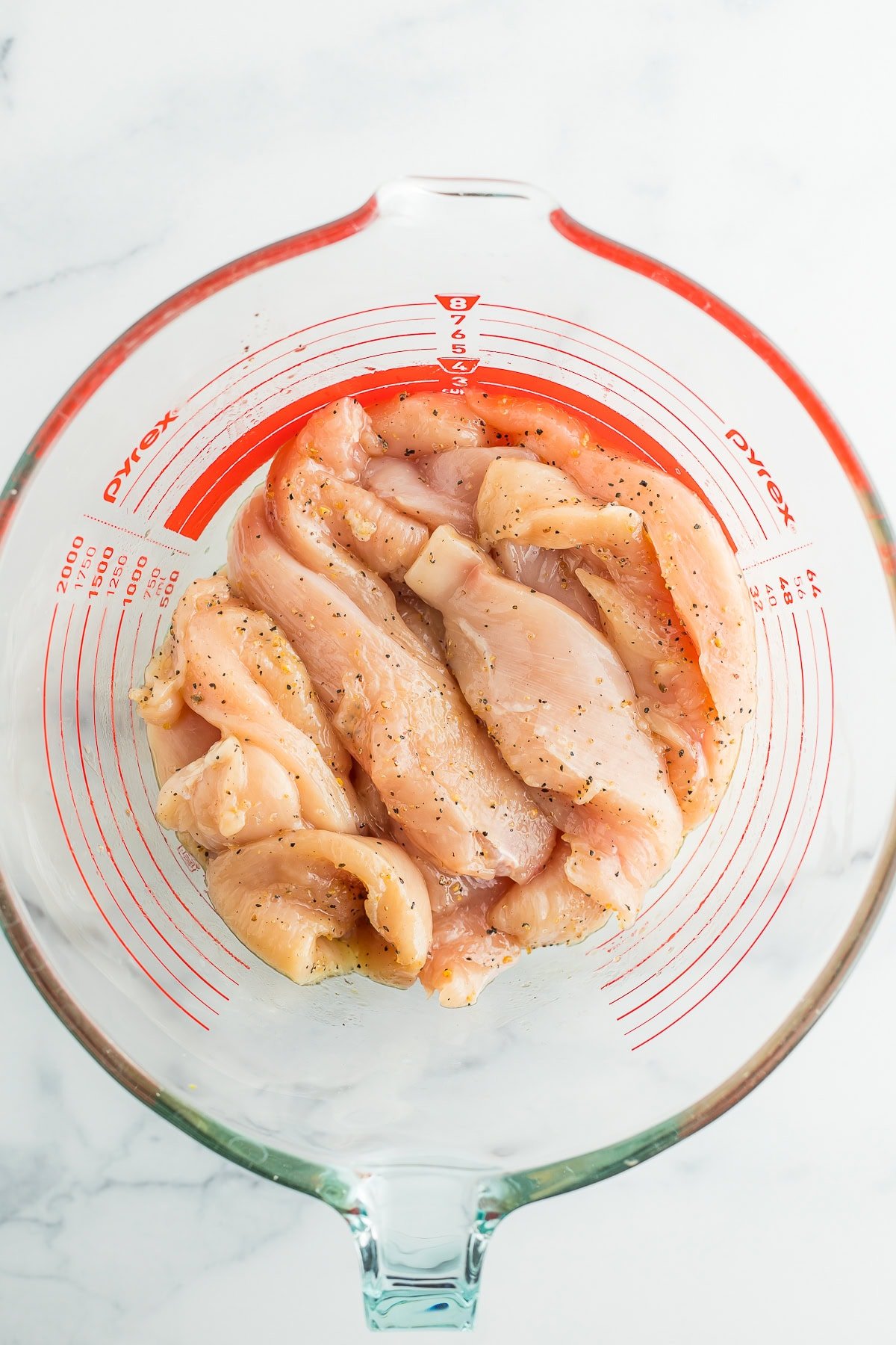 a glass bowl with seasoned uncooked chicken.