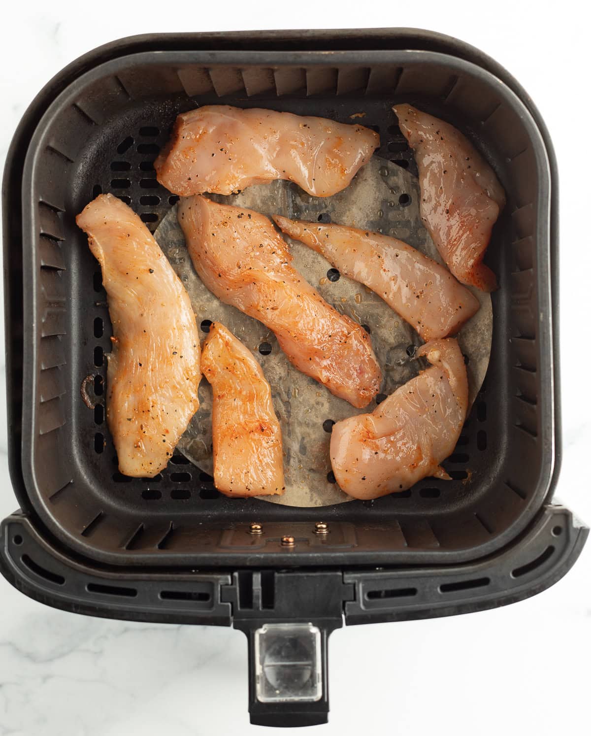uncooked chicken breasts in an air fryer.