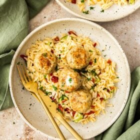 chicken meatballs topping a plate of orzo pasta with herbs.