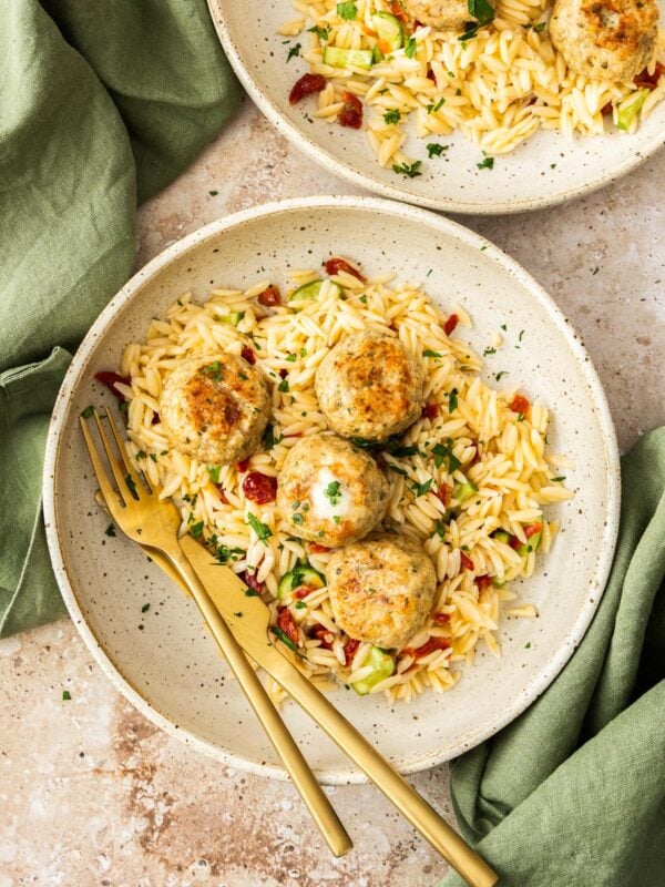 chicken meatballs topping a plate of orzo pasta with herbs.