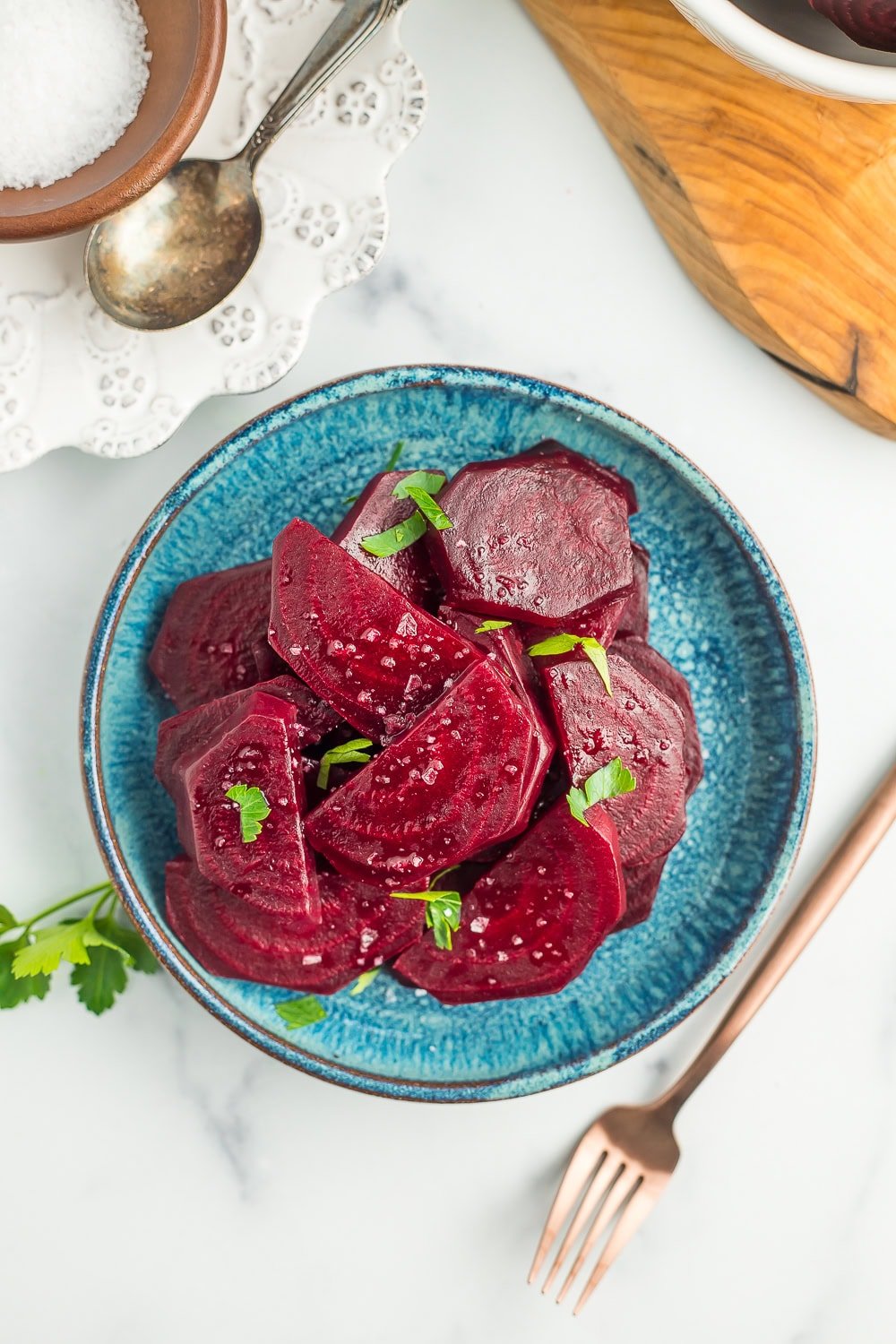 a teal plate with sliced beets topped with flaky sea salt and chopped parsley.