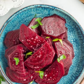 a teal plate with sliced beets topped with flaky sea salt and chopped parsley.