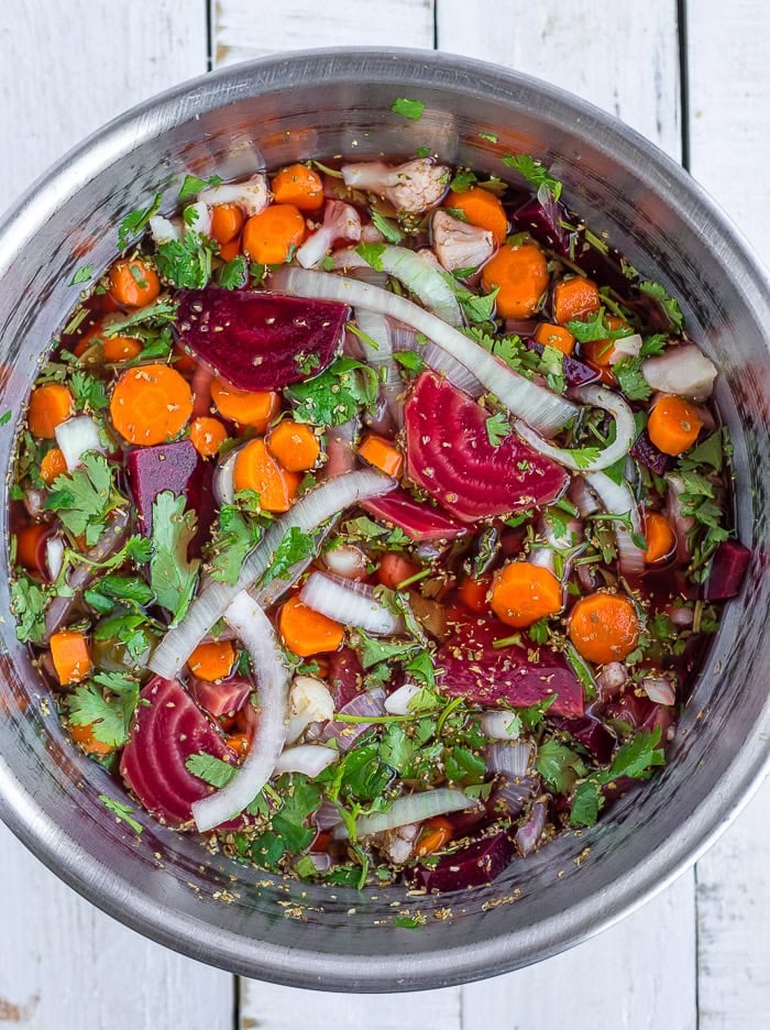 a large stainless bowl with slices of beets, onions, carrots, and cauliflower.
