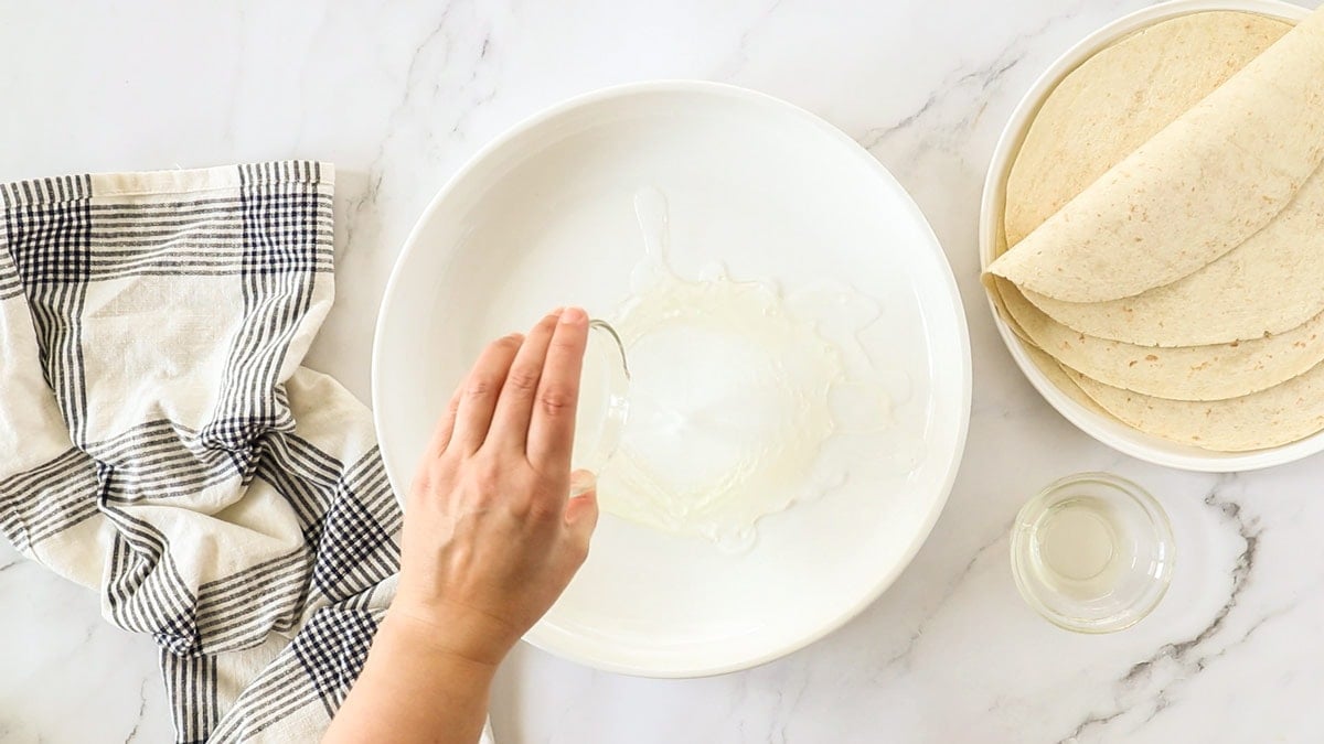 a hand pour water and oil into a white bowl.